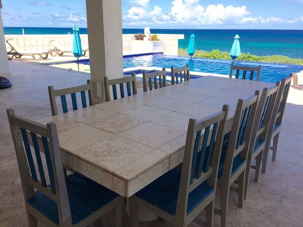 Comedor con vista a la piscina, sillas y sombrillas exteriores.