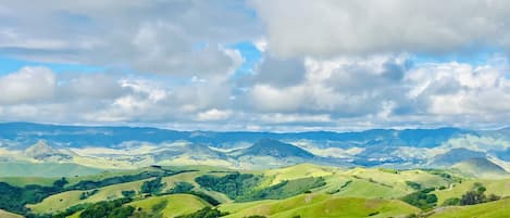 A panoramic view of rolling green hills and distant mountains under a partly cloudy sky.