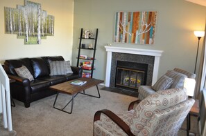 A living room with a fireplace, a black leather sofa, a patterned armchair, a coffee table, and a bookshelf. - Family-Friendly 3 BR House - Short Walk to Downtown Louisville, Trails & Park (Louisville)