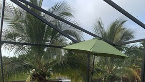 Een terras met een zwembad, tuinmeubilair en uitzicht op palmbomen en water.