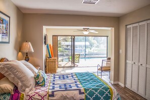 A bedroom with a bed, a lamp, a window, and a view of a pool and outdoor seating. - Vacation in paradise !! (Cape Coral)