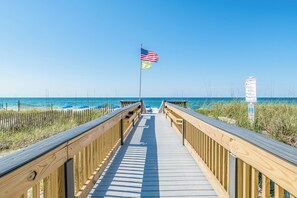 A wooden boardwalk leading to the beach with an American flag and a warning sign.