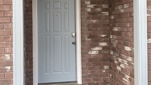 A white door with a keypad lock, set in a brick wall with a white trim and a small light fixture above.