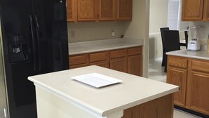 A kitchen with wooden cabinets, a black refrigerator, a white countertop, and a blender.
