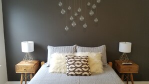 Une chambre à coucher comprenant un lit, deux tables de chevet, un luminaire suspendu et une étagère fixée au mur.
