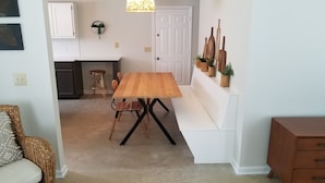 Un coin repas avec une table et des chaises en bois, un banc, et une cuisine en arrière-plan.