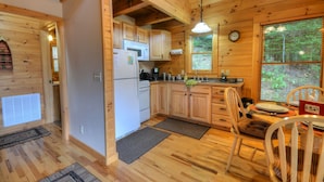 A wooden cabin kitchen with a refrigerator, stove, cabinets, and a dining table with chairs.
