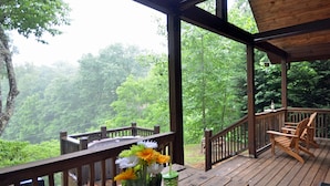 A wooden deck with a railing, a table with a drink and flowers, and chairs.