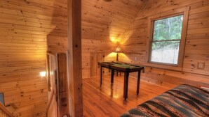 A wooden cabin interior with a pool table, a lamp, and a window with blinds.