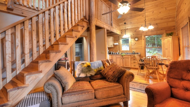A wooden interior with a staircase, a sofa with patterned cushions, a dining area, and a kitchen.