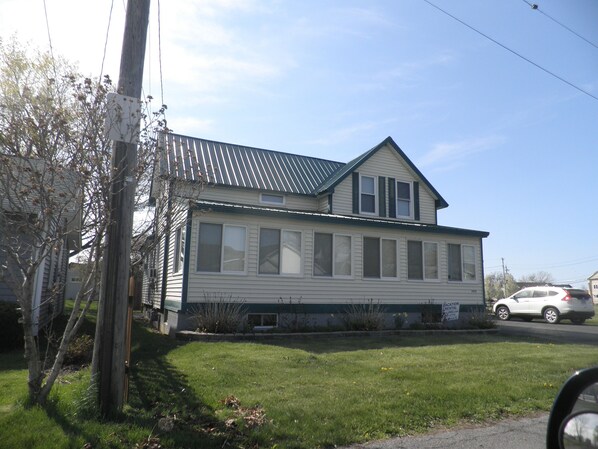 A two-story house with a metal roof, large windows, and a grassy yard. - Amazing Lake View Cottage with Game room for Kids of all ages (Sodus Point)