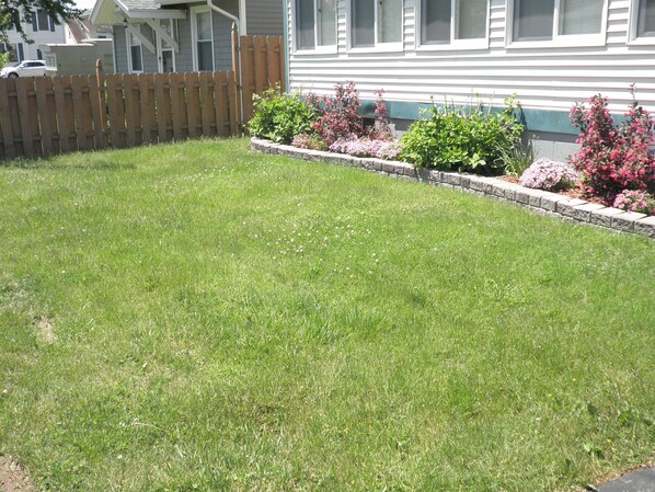 A well-maintained lawn with a wooden fence and flower beds in front of a house.