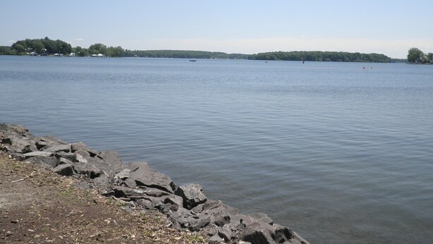 A calm lake with rocky shores and a distant shoreline with trees and buildings. - Amazing Lake View Cottage with Game room for Kids of all ages (Sodus Point)