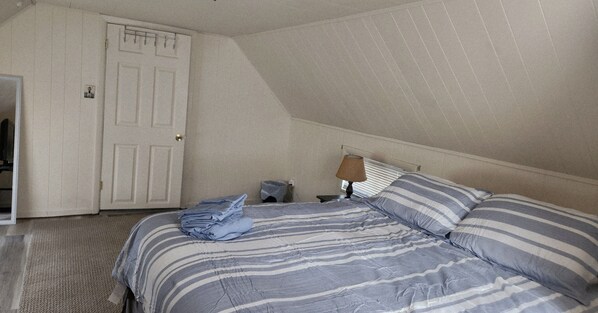 A bedroom with a bed, a nightstand, a lamp, a door, and a window.