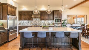 Une cuisine moderne avec des meubles en bois, des appareils en acier inoxydable, un grand îlot central doté de tabourets, un éclairage suspendu et une vue sur la salle à manger.