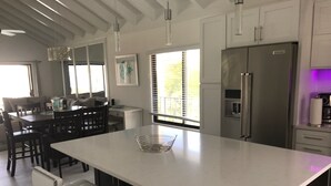 A modern kitchen with a large island, dark wooden chairs, and a refrigerator.