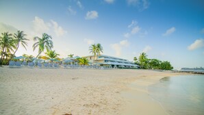A beachfront hotel with palm trees, sun loungers, and a clear sky.