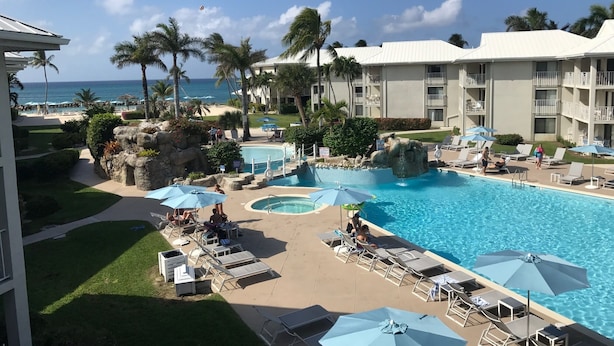 A resort pool area with multiple pools, lounge chairs, umbrellas, and palm trees.