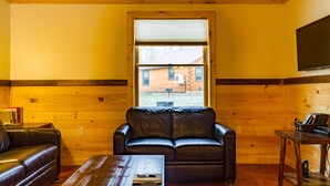 A cozy room with wooden walls, a black leather sofa, a wooden coffee table, and a window with blinds. - Rustic yet Modern Log Cabin, Cayuga Wine Trail, Dog Friendly, Open Year Round (Ovid)
