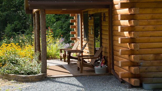 A log cabin with a porch, wooden chairs, and a gravel pathway. - Rustic yet Modern Log Cabin, Cayuga Wine Trail, Dog Friendly, Open Year Round (Ovid)