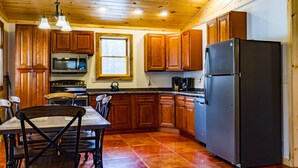 A kitchen with wooden cabinets, a refrigerator, a stove, and a dining table with chairs. - Rustic yet Modern Log Cabin, Cayuga Wine Trail, Dog Friendly, Open Year Round (Ovid)