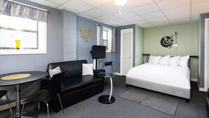 Una habitación de hotel con una cama, un sofá de cuero negro, una mesita redonda pequeña, un televisor y un ventilador de techo.