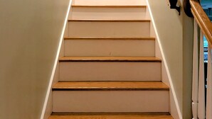 A staircase with wooden steps and white walls, leading to a door at the top.