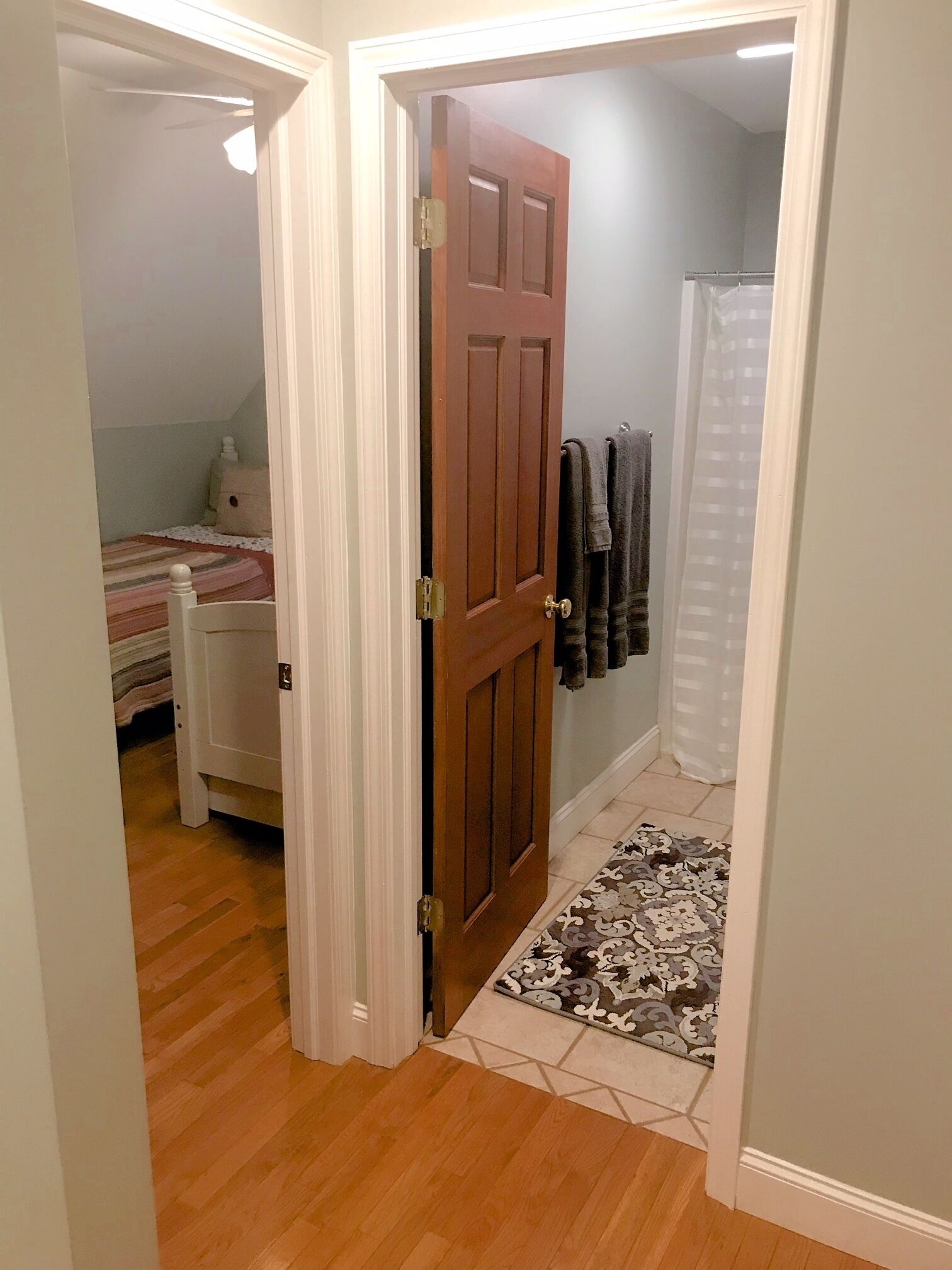 Une chambre à coucher comprenant un lit, une table de chevet et une porte donnant sur une salle de bain équipée d’un rideau de douche.