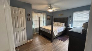 Une chambre à coucher avec un lit à baldaquin, un ventilateur de plafond, une fenêtre avec des stores et une commode.