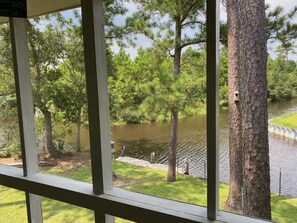 A view through a window with a wooden frame, overlooking a grassy area with trees and a body of water. - Relaxing Waterfront Getaway with Fenced in Pet Friendly Property (Bay St Louis)