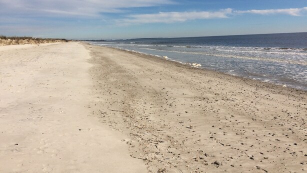 Ein sandiger Strand mit sanften Wellen und blauem Himmel.