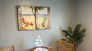 Ein Zimmer mit zwei Holzstühlen, einem kleinen runden Tisch mit einem Modell eines Segelbootes und einer großen Küstpflanze.