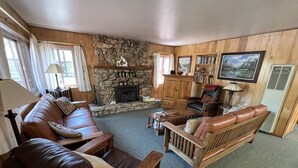 A cozy living room with a stone fireplace, leather sofas, wooden furniture, and a bookshelf.