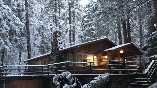 A wooden cabin with a stone chimney, surrounded by snow-covered trees.