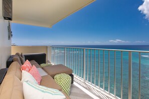 A balcony with a sofa and cushions, overlooking a clear blue sea.