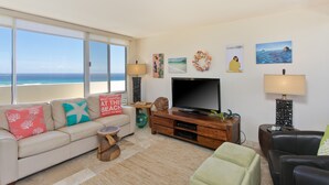 Ett vardagsrum med en stor TV, en soffa, ett soffbord och utsikt över havet.