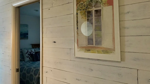 A room with a wooden wall, a framed picture of a window, and a door leading to another room.