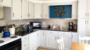 A kitchen with white cabinets, a microwave, a toaster, a kettle, a sink, and a coffee maker.