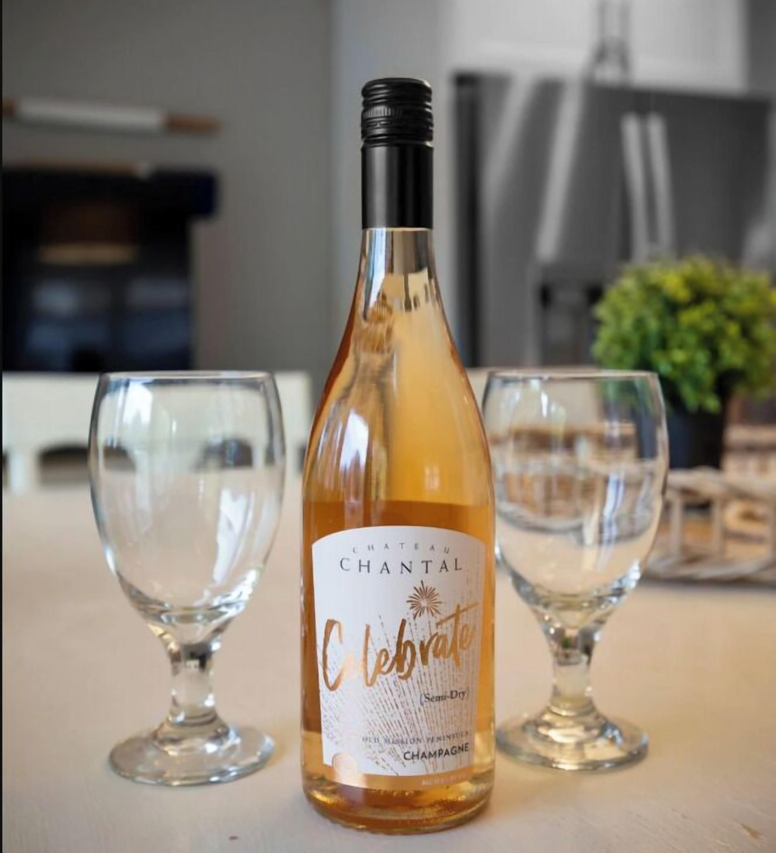 A bottle of Chantal Chantal semi-dry champagne with two empty wine glasses on a table.