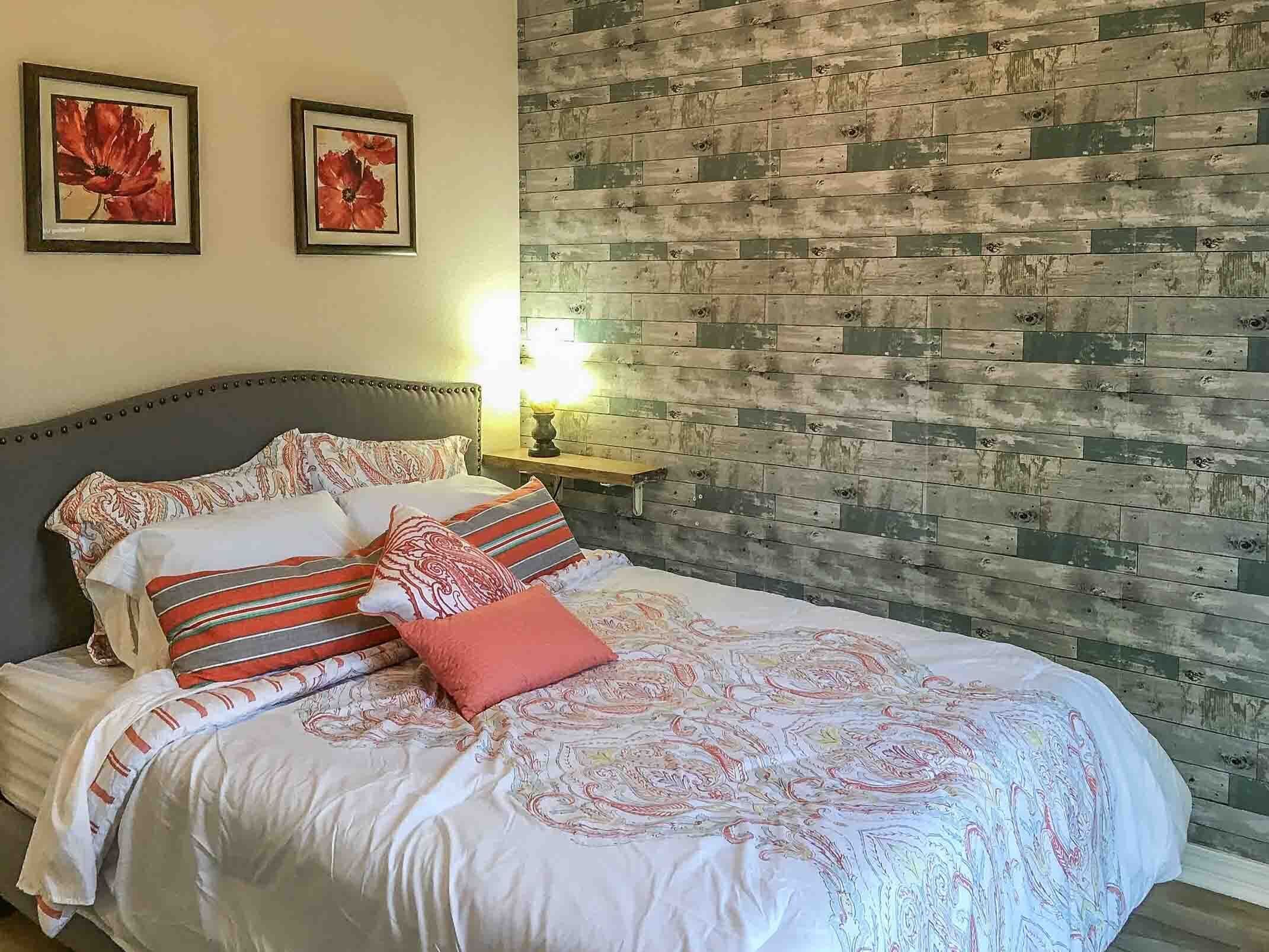 A bed with patterned bedding, two framed floral artworks on the wall, and a wooden plank wall.