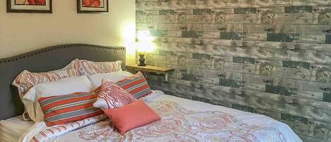 A bed with patterned bedding, two framed floral artworks on the wall, and a wooden plank wall.