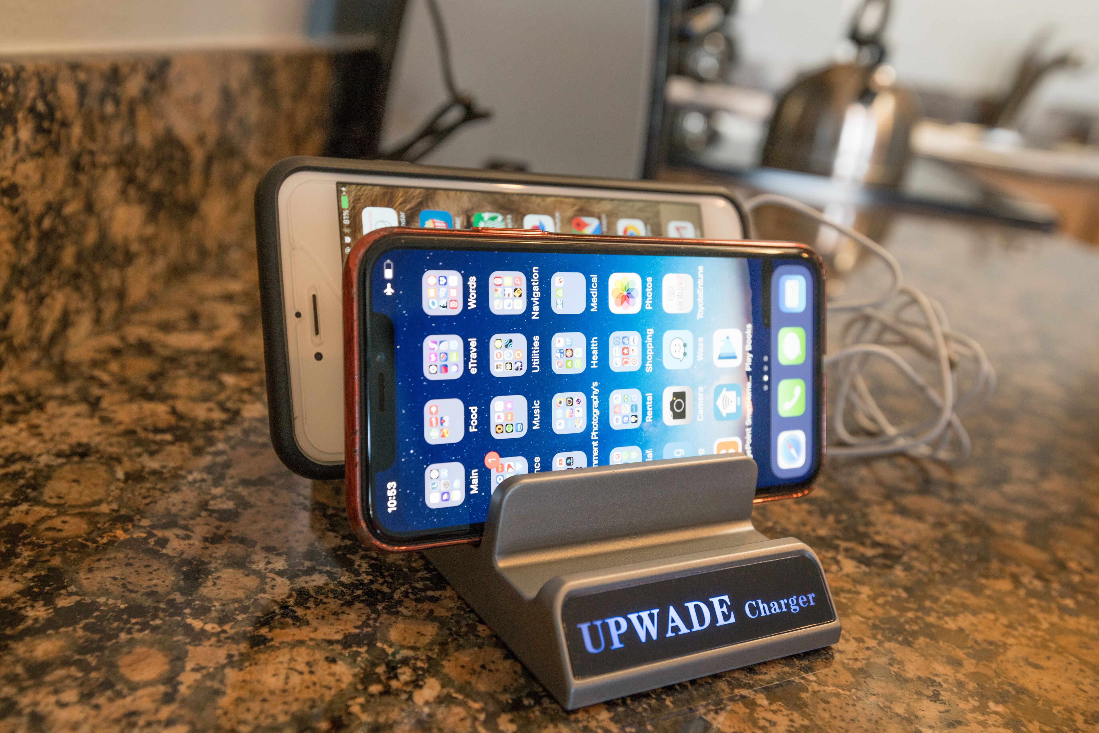 Two smartphones charging on a granite countertop with a label reading "UPWADE Charger".