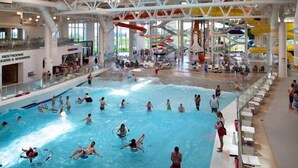 Una piscina interior con varias pistas de natación, un tobogán acuático y una zona de estar a un lado.