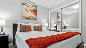 Una habitación de hotel moderna con una cama grande, una manta roja y un espejo amplio.