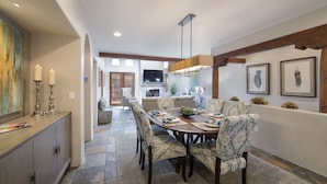 A dining area with a long table, patterned chairs, and a chandelier. There is a television in the background and a fireplace. - In The Heart Of Santa Fe, Walk to Everything Downtown, 3 Bed, 3 Bath Townhouse (Santa Fe)