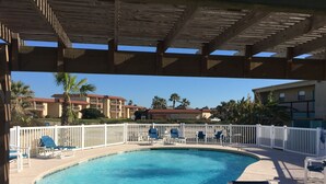Un área de piscina con una pérgola de madera, rodeada de vallas blancas y sillas de descanso azules.