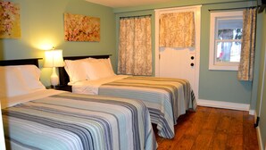 Habitación de hotel con dos camas, una mesita de noche con lámpara, cortinas con motivos florales y una ventana con vistas al exterior.
