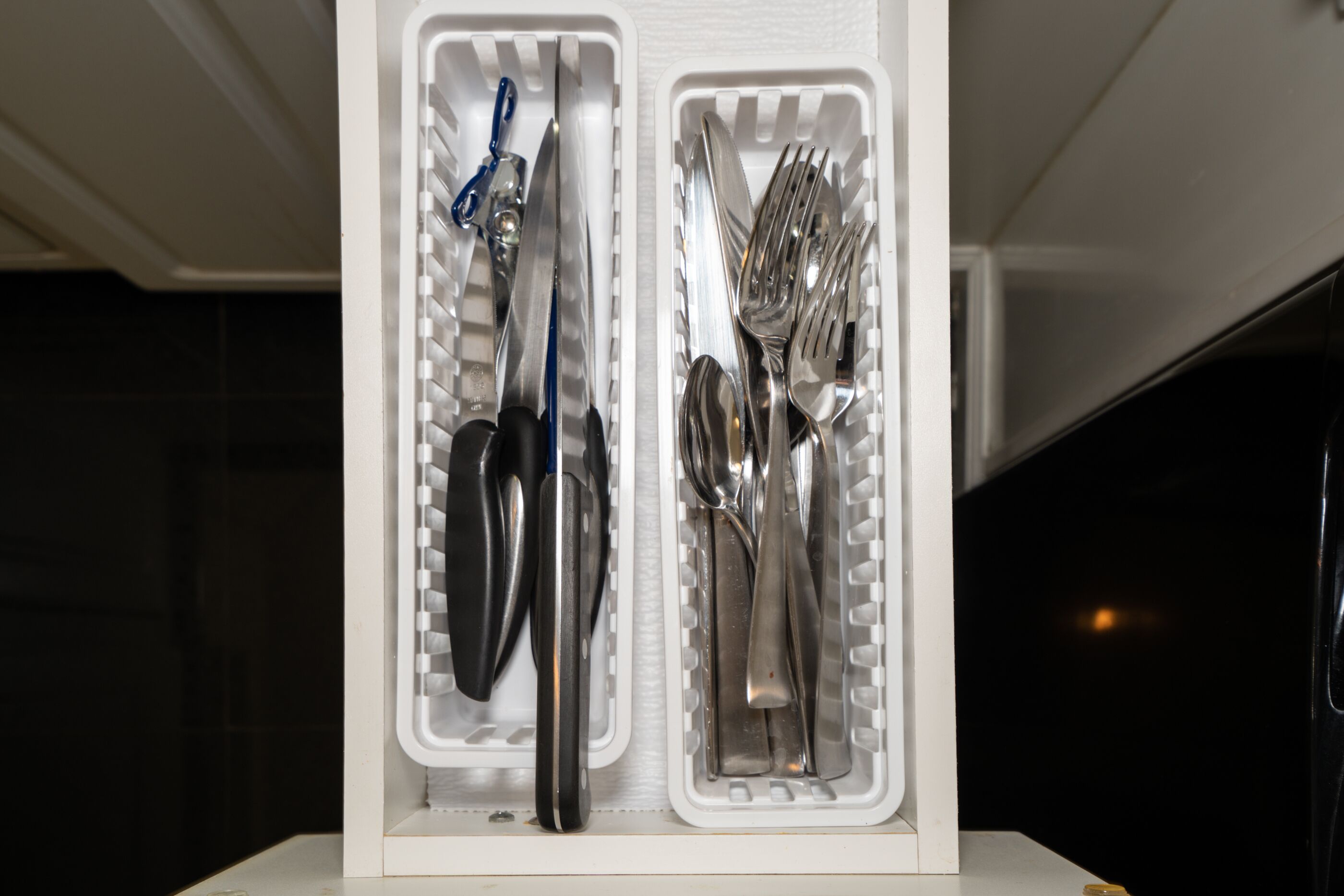 Una caja blanca de almacenamiento con compartimentos que contienen diversos utensilios de cocina, como cuchillos, tenedores y cucharas.