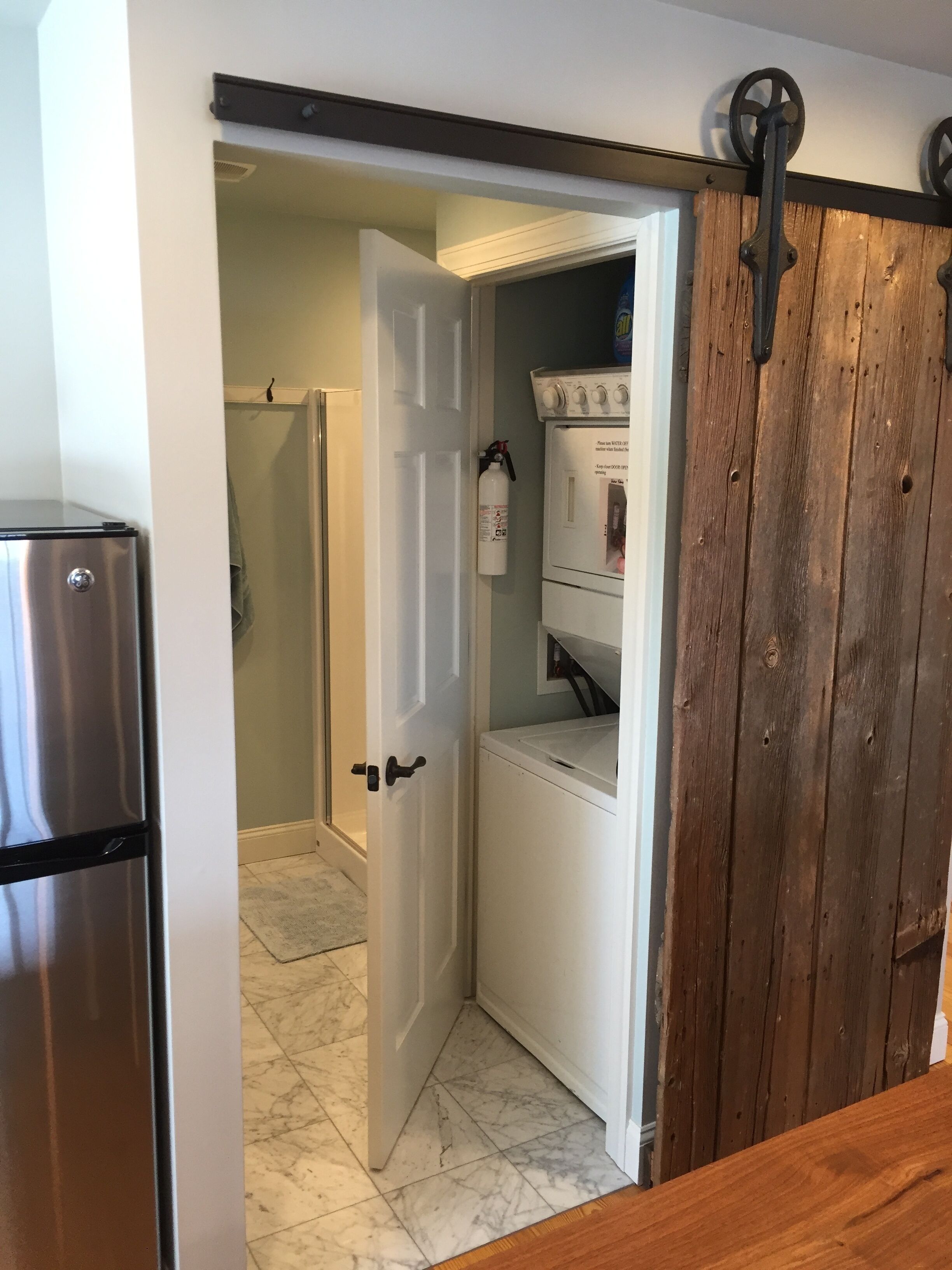 A laundry room with a washing machine, dryer, and a door leading to a bathroom with a shower.