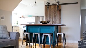 A kitchen with a blue island, bar stools, and a rustic wooden door.